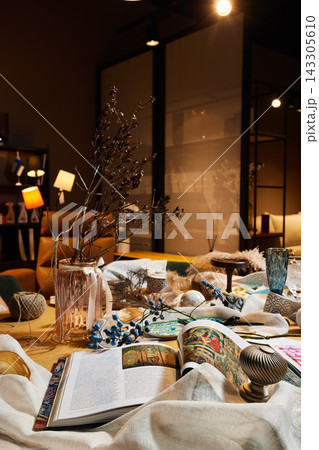 Warm evening table scene with dried branches in glass vase, open magazine, ceramic dishes, patterned textiles, ambient lamps, and cozy decor creating inviting home dining ambiance Warm evening table scene with dried branches in glass vase, open magazine, ceramic dishes, patterned textiles, ambient lamps, and cozy decor creating inviting home dining ambiance 143305610