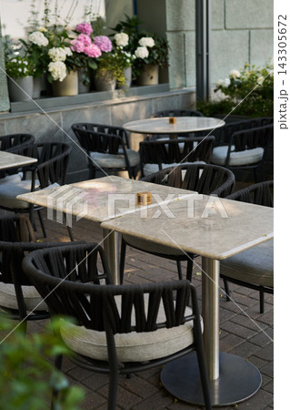 Outdoor cafe tables with woven rope chairs, potted hydrangeas on windowsill, marble tabletops on brick pavement, cozy urban terrace for restaurant or hospitality use 143305672