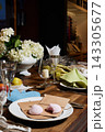 Cozy dining table with white hydrangea bouquet, pink macarons on parchment, crystal glasses, folded napkins, candle glow, assorted cutlery on wooden tabletop Cozy dining table with white hydrangea bouquet, pink macarons on parchment, crystal glasses, folded napkins, candle glow, assorted cutlery on wooden tabletop 143305677