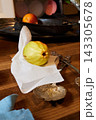 Golden apple rests on white napkin beside weathered wooden table with tarnished silverware and dark metal pan in cozy kitchen still life, warm light highlighting fruit skin textures Golden apple rests on white napkin beside weathered wooden table with tarnished silverware and dark metal pan in cozy kitchen still life, warm light highlighting fruit skin textures 143305678