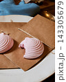 Pink macarons on kraft parchment with twine, resting on rustic table setting beside brass spoon, against blue fabric background in warm kitchen light Pink macarons on kraft parchment with twine, resting on rustic table setting beside brass spoon, against blue fabric background in warm kitchen light 143305679