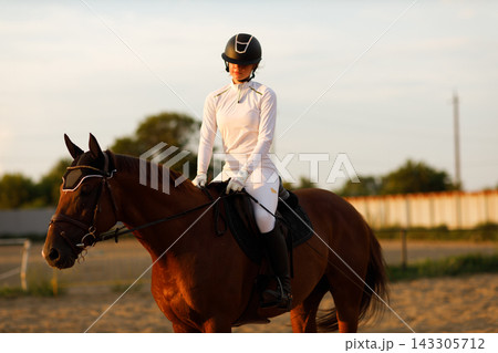 Woman rider jockey in helmet and white uniform preparing horse racing. Woman rider jockey in helmet and white uniform preparing horse racing. 143305712