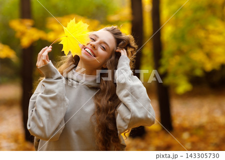 Young laughing woman holds yellow leaf in her hand in the park at sunset. 143305730