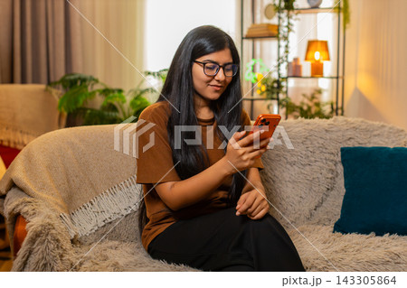 Indian woman on home sofa calmly checking smartphone messages during relaxed online browsing indoors 143305864