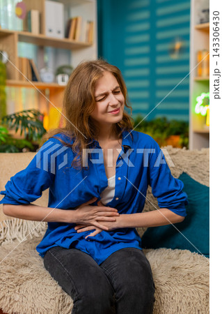 Young woman on home sofa feeling stomach pain and discomfort with painful expression indoors at home Young woman on home sofa feeling stomach pain and discomfort with painful expression indoors at home 143306430