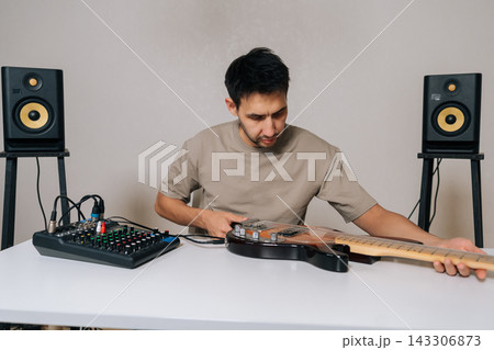 Musician connecting electrical bass guitar to audio mixer with cables, preparing to record or perform music, surrounded by studio monitors for sound production, copy space, isolated background. Musician connecting electrical bass guitar to audio mixer with cables, preparing to record or perform music, surrounded by studio monitors for sound production, copy space, isolated background. 143306873