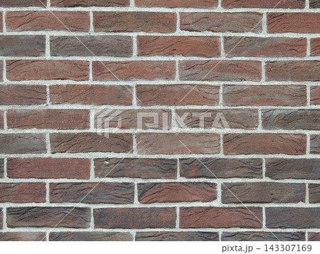 Rustic-style brick wall texture. Red and brown facing brick with a textured surface and gray cement mortar joints. Background for design, architecture, construction, and loft-style interiors.  143307169