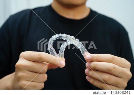 Man holding invisible aligner orthodontic retainer for dental teeth straightening. Man holding invisible aligner orthodontic retainer for dental teeth straightening. 143308241