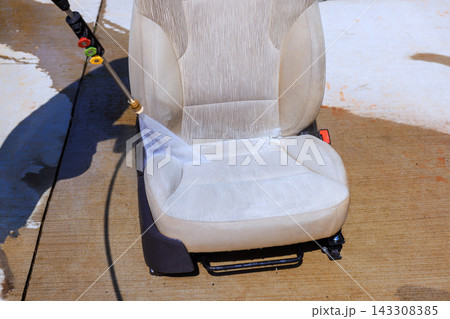 Water is sprayed on dirty car seat in driveway while cleaning. Water is sprayed on dirty car seat in driveway while cleaning. 143308385