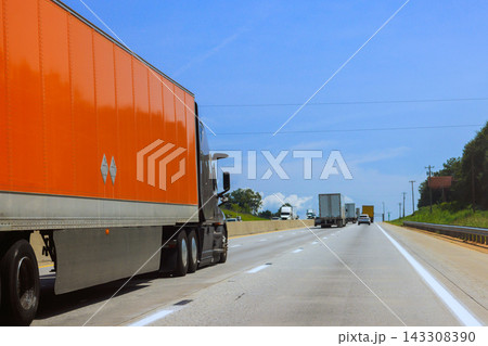 Large trucks drive on wide interstate highway with clear skies few clouds visible in distance. 143308390