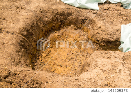 A freshly dug hole in the ground shows prepared soil for planting purposes, surrounded by loose earth. 143309378