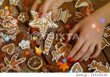 Woman decorates a festive christmas table with gingerbread cookies. Hands hold tasty cookies in form of heart or love shaped. Woman decorates a festive christmas table with gingerbread cookies. Hands hold tasty cookies in form of heart or love shaped. 143310136