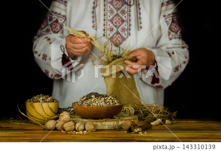 Woman in ukrainian native dress with Christmas porridge kutya. Woman in ukrainian native dresses standing behind table with kutia. Woman in ukrainian native dress with Christmas porridge kutya. Woman in ukrainian native dresses standing behind table with kutia. 143310139