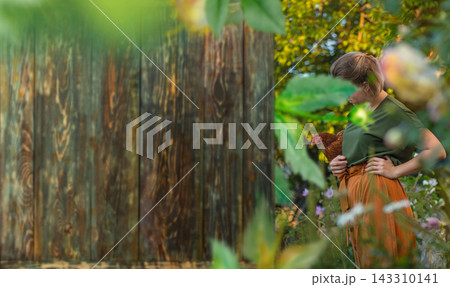 Caretaker gently gathers hen from nesting area close to coop entrance. Woman stands with laying hen close to henhouse in countryside setting. Extra wide banner Caretaker gently gathers hen from nesting area close to coop entrance. Woman stands with laying hen close to henhouse in countryside setting. Extra wide banner 143310141