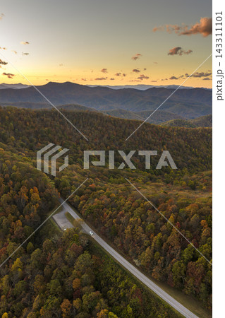 Car traveling on winding forest road during fall season at sundown. Vehicle driving through mountain woods under glowing autumn leaves. Car traveling on winding forest road during fall season at sundown. Vehicle driving through mountain woods under glowing autumn leaves. 143311101
