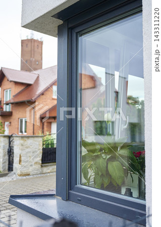 Modern house window with dark frame, wet sill and indoor plant behind glass 143311220