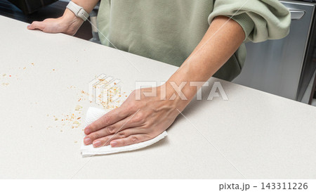 Woman wiping crumbs from kitchen table with hand, homemade baking process, food preparation routine, cozy home cooking lifestyle. 143311226