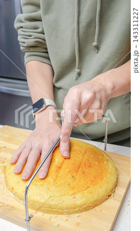 Person using a cake leveler to slice a round cake on a wooden cutting board in a modern kitchen setting Person using a cake leveler to slice a round cake on a wooden cutting board in a modern kitchen setting 143311227