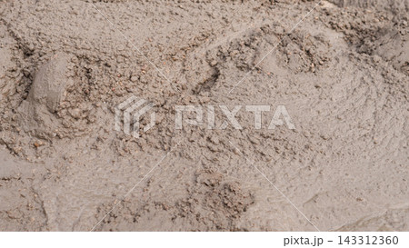 Close view of wet muddy soil with rough clumps, ripples, and soft earthy tones, creating raw natural texture for background, surface detail, construction, agriculture, and outdoor material concepts. Close view of wet muddy soil with rough clumps, ripples, and soft earthy tones, creating raw natural texture for background, surface detail, construction, agriculture, and outdoor material concepts. 143312360