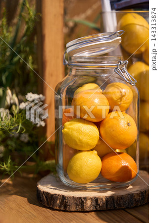 Glass Jar Filled With Lemons And Oranges On Wood Slice In Garden Display 143313874