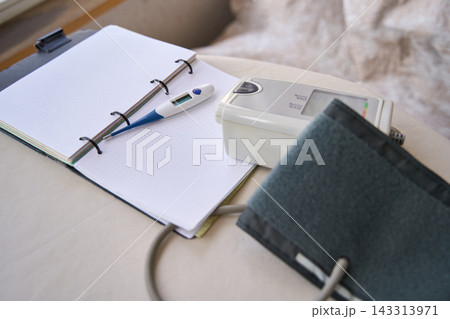 Health Diary With Digital Thermometer And Blood Pressure Cuff Arranged On Bedside Desk Beside Open 143313971