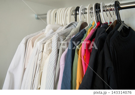 Row Of White And Colored Shirts Hangs From Mixed Hangers On Metal Wardrobe Rail, With Black Row Of White And Colored Shirts Hangs From Mixed Hangers On Metal Wardrobe Rail, With Black 143314076