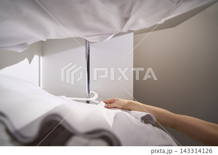 Hand Reaches For White Shirt On Hanger From Beneath Hanging Garments, With Open Wardrobe Door Hand Reaches For White Shirt On Hanger From Beneath Hanging Garments, With Open Wardrobe Door 143314126
