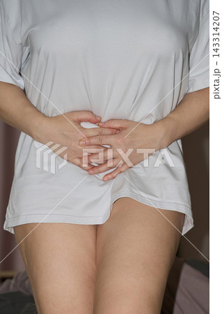Overlapping Hands Press Against Lower Abdomen Through Loose White Shirt, With Bare Thighs 143314207