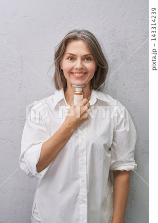 Smiling Woman Holding Handheld Neck Massage Device Against Gray Studio Wall In Casual Wellness 143314239