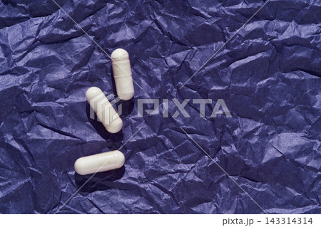White Capsules Arranged In Scattered Trio On Crumpled Dark Blue Paper Surface With Directional White Capsules Arranged In Scattered Trio On Crumpled Dark Blue Paper Surface With Directional 143314314