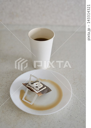 Tea Bag Resting On White Plate With Brown Ring Stain In Front Of Filled Paper Cup On Speckled Tea Bag Resting On White Plate With Brown Ring Stain In Front Of Filled Paper Cup On Speckled 143314321