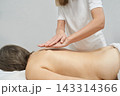 Female Massage Therapist Gliding Hands Across Client Back In Bright Treatment Room With White 143314366
