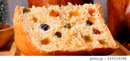 Traditional Christmas panettone presented as a generous slice, highlighting the soft dough, candied fruit, in a festive setting. Traditional Christmas panettone presented as a generous slice, highlighting the soft dough, candied fruit, in a festive setting. 143314596