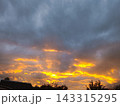Dramatic sunset sky with intense yellow light shining through heavy dark clouds. Silhouettes of trees and roofline 143315295