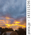 Vertical photo of dramatic sunset sky with bright yellow light breaking through dark clouds. Silhouettes of trees and greenhouse 143315296