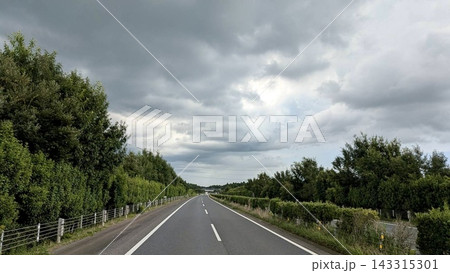 厚い雲の下をまっすぐ伸びる緑に囲まれた高速道路 143315301