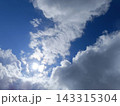 Bright blue sky with fluffy white and grey clouds. Sun shining brightly through cloud cover 143315304