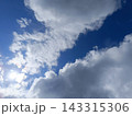 Bright blue sky partially covered by fluffy white and grey clouds. Intense sunlight shining from behind clouds 143315306
