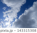 Bright sun shining through fluffy white cumulus clouds in a blue sky. Sunny day weather background 143315308