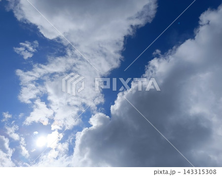 Bright sun shining through fluffy white cumulus clouds in a blue sky. Sunny day weather background 143315308