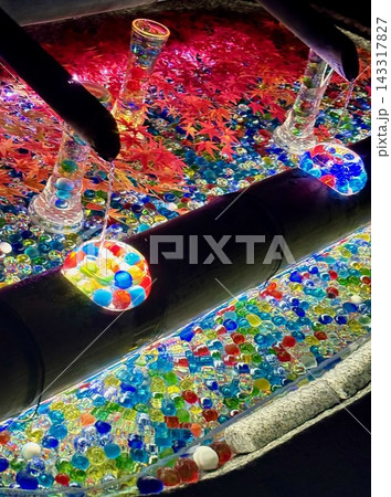 ライトアップされた鮮やかなガラス玉と紅葉の花手水⁠ ⁠夜の境内に輝くカラフルなおはじきと清涼感ある手 143317827