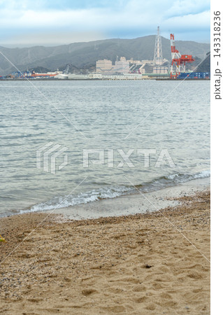 穏やかな波が寄せる砂浜と海越しに望む対岸の港湾 穏やかな波が寄せる砂浜と海越しに望む対岸の港湾 143318236
