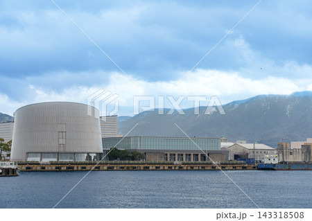 海越しに広がる近代的な建築物と背景に山並みがそびえる港町の風景 143318508