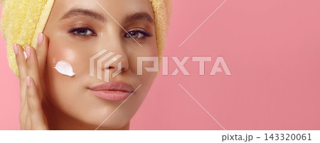 Young woman applies lotion on cheek showing blank tube 143320061
