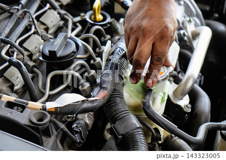 Mechanic hand performing maintenance by checking coolant reservoir in a car engine Mechanic hand performing maintenance by checking coolant reservoir in a car engine 143323005