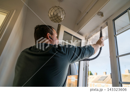 Cleaning the window. A man with steam device removes dirt from the plastic window frame. Cleaning the window. A man with steam device removes dirt from the plastic window frame. 143323606