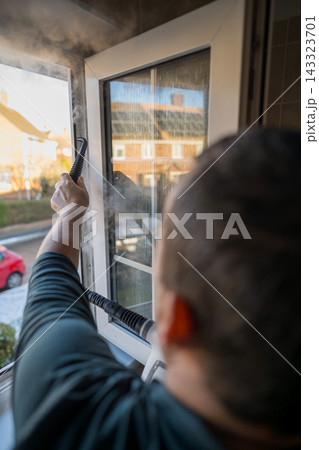 Cleaning the window. A man with steam device removes dirt from the plastic window frame. 143323701