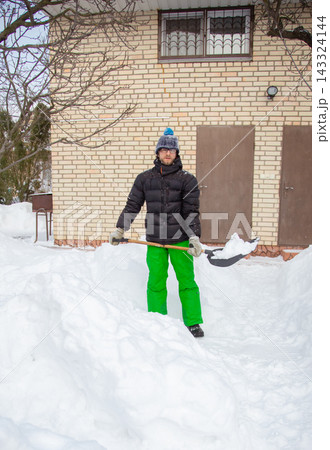 Man in winter jacket shoveling snow with shovel in front of brick house Man in winter jacket shoveling snow with shovel in front of brick house 143324144