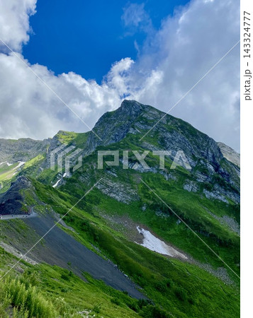 Dramatic green mountain peak rises beneath sweeping white clouds in summer. Dramatic green mountain peak rises beneath sweeping white clouds in summer. 143324777