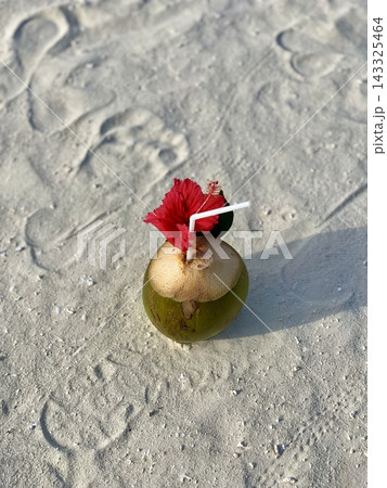 Fresh coconut drink with red hibiscus flower standing on sunlit beach sand. Fresh coconut drink with red hibiscus flower standing on sunlit beach sand. 143325464